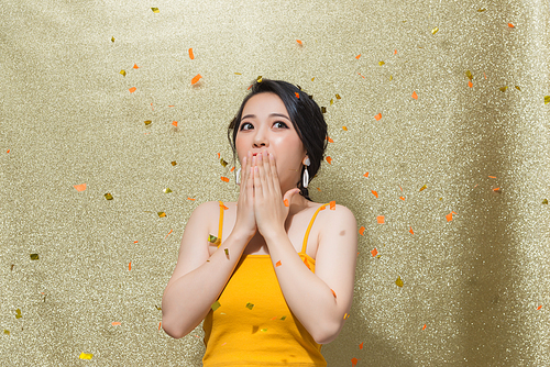 Portrait of beautiful young woman with party whistle and falling confetti on color background