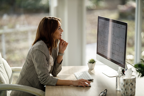 A smiling business woman sitting alone in her home office and working on computer.