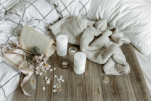 Cozy home still life with candles, knitted element, book and flowers.