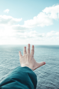 Hand of a man over a crystal clear horizon of the ocean with white clouds with copy space, inspiration and freedom concept