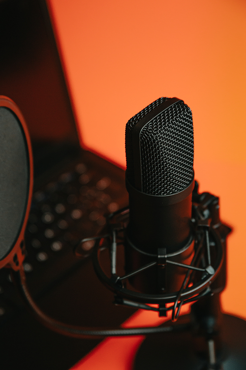 Close up mock up of a streaming microphone with a laptop over an orange background with copy space, minimal concept, technology streaming