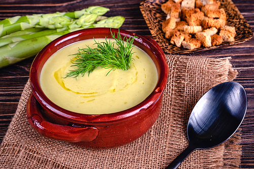 Fresh asparagus creamy soup and ingredients on wooden table on rustic wooden background, selective focus