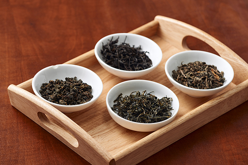 the white drinking bowls of assortment of dry tea in order on wooden background