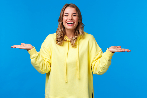 Happy carefree good-looking woman, blonde short haircut, holding both hands raised sideways as if holding two products, give you choice and laughing, introuce two products, blue background.