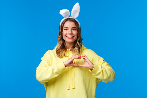 holidays, traditions and celebration concept. waist-up portrait of charismatic cute blond girl in rabbit ears, congratulate everyone with . holiday, show heart gesture and smiling.