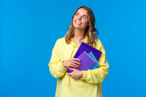 Back to school. Cute blond smiling european female student carry notebooks and learning material, look dreamy upper left corner smiling, thinking what she grab for lunch, blue background.