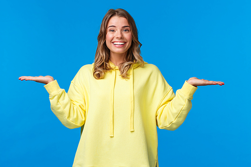 Carefree happy smiling woman weighing something in arms, as if holding two products, look camera suggest make choice, deciding between variants, stand blue background.