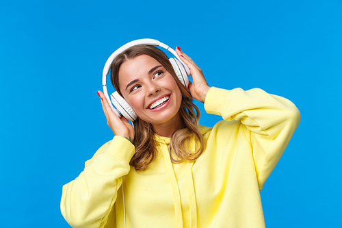 Music, lifestyle and youth concept. Close-up portrait dreamy good-looking cute blond girl with short haircut, listening songs, favorite playlist in headphones, dancing looking up smiling pleased.