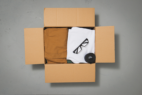 Cardboard donation box with clothes on gray background