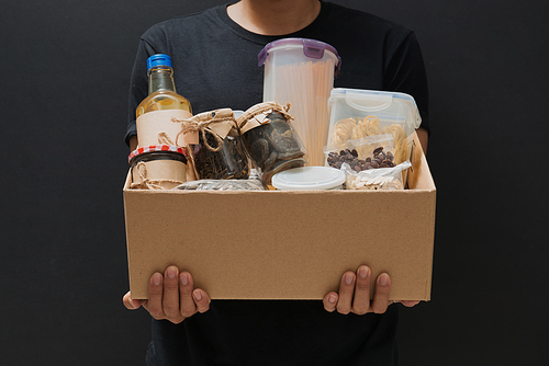 A man holding a donation box of different products on dark background
