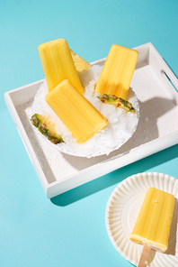 Pineapple ice pops on a tray. Top view scene over a blue background