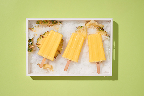 Yellow fruit popsicles on a tray top view, summer mood