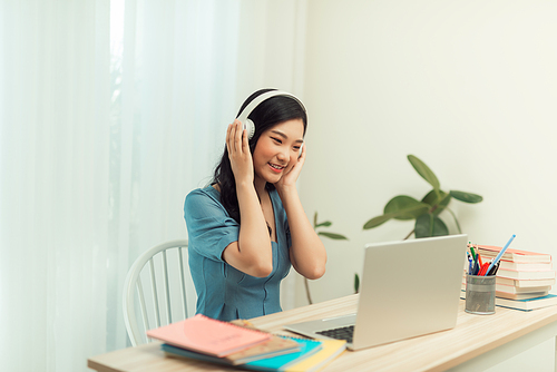 Dedicated female freelancer in glasses and wireless headphones smiling at camera while sitting at laptop with mug