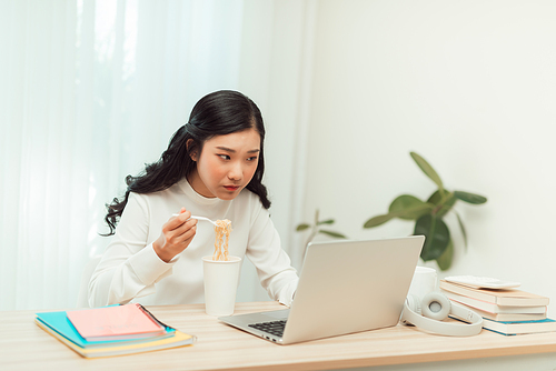 Asia freelance business woman eating instant noodles while working on laptop in living room at home office