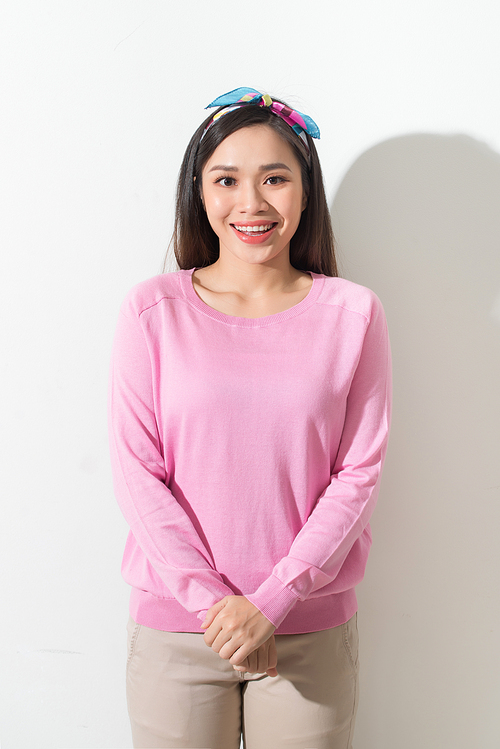 a smiling young asian woman standing and looking at camera over gray background