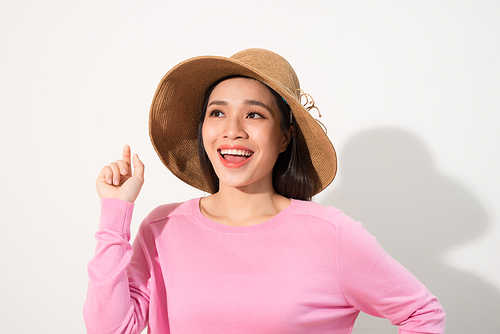 Beautiful young woman in pink dress and sun hat is pointing at copy space, shouting and looking at camera.