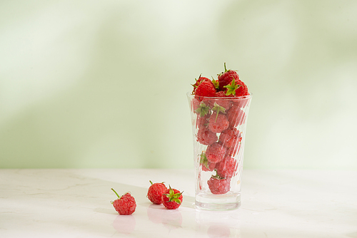 Fresh raspberries in a glass beaker isolated on light background