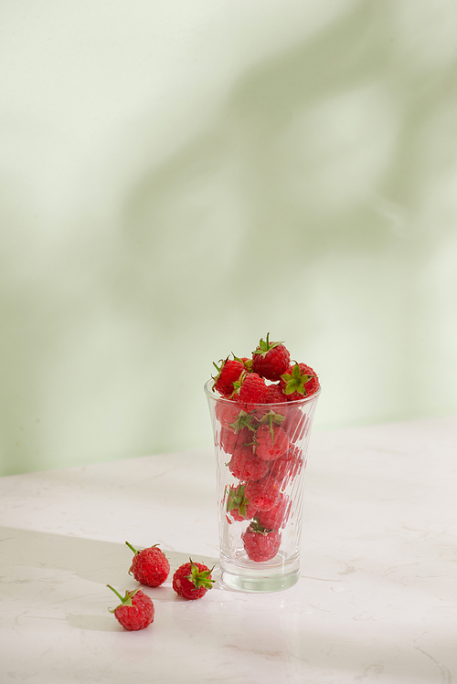 Fresh raspberries in a glass beaker isolated on light background