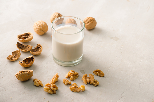 Organic walnut nuts and glass of walnut milk on stone background.