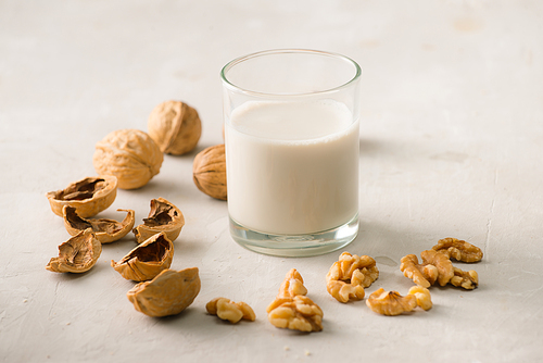 Organic walnut nuts and glass of walnut milk on stone background.