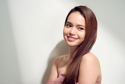 Elegant asian girl with tanned skin posing with pensive face expression on bright background.