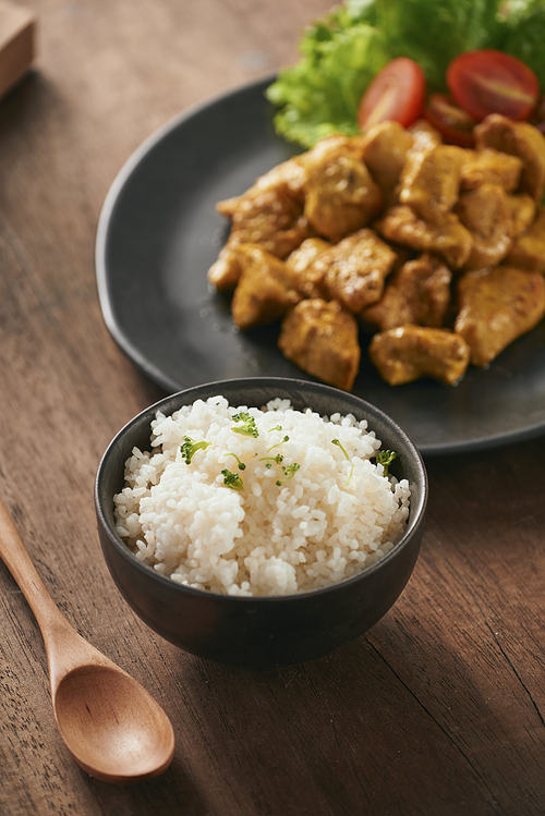 White rice with curry and chicken in black plate on wooden table