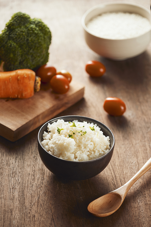 Grains of rice in a wooden bowl and ingredients for a vegetarian recipe - healthy eating concept