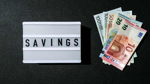 Lightbox board with word SAVINGS in black letters around Euro banknotes. Money, Business, finance, investment, saving. Cash bill. Business budget of wealth and prosperity finance