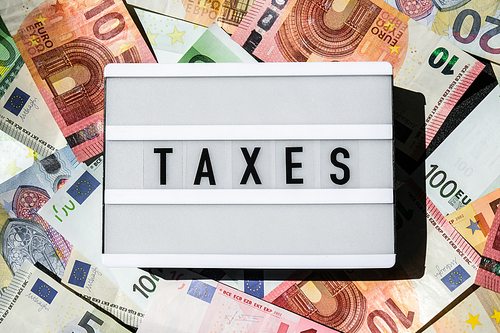 Lightbox board with word TAXES in black letters around Euro banknotes. Tax payment and filing concept. Money, Business, finance, investment, saving and corruption. Cash bill