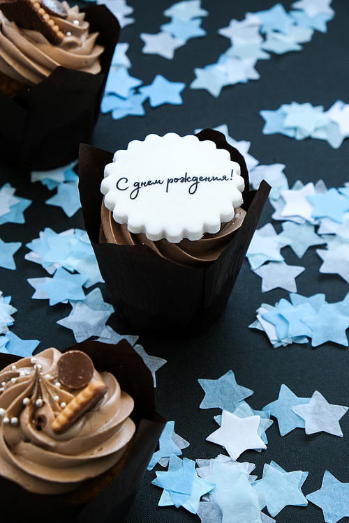Happy birthday written in Russian on Delicious chocolate cupcake with cream on dark background. Muffin. Birthday cake party. Homemade Chocolate Cupcake