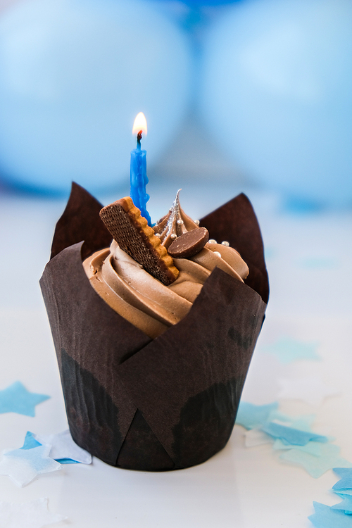 Sweet tasty chocolate cupcake with candle on blue festive background. Happy Birthday party concept. Delicious birthday cake. Boy or girl party.