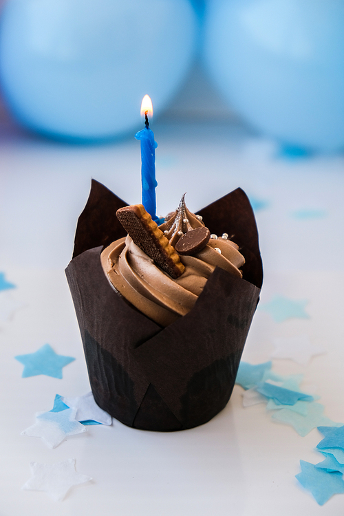 Sweet tasty chocolate cupcake with candle on blue festive background. Happy Birthday party concept. Delicious birthday cake. Boy or girl party.