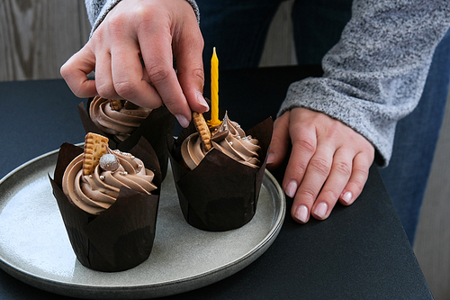Female hands making Delicious chocolate cupcakes with cream on dark background. Three chocolate muffin. Birthday cake party preparation. Homemade Chocolate Cupcake