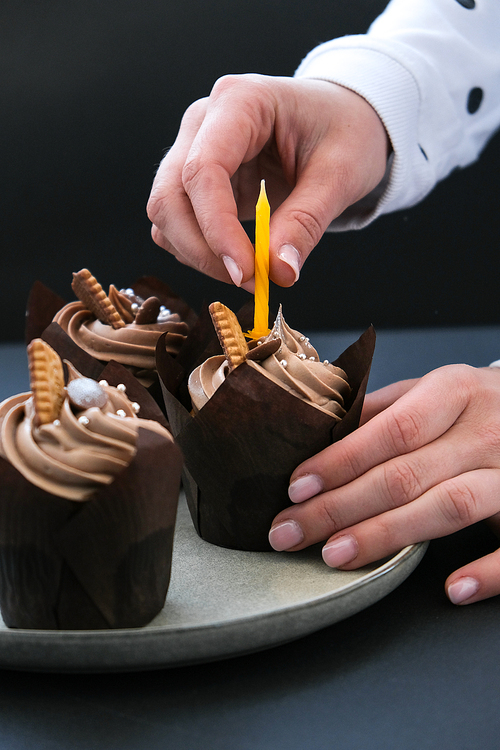 Female hands making Delicious chocolate cupcakes with cream on dark background. Three chocolate muffin. Birthday cake party preparation. Homemade Chocolate Cupcake