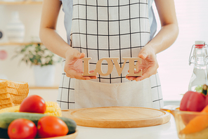 A woman holding wooden letter LOVE while cooking in the kitchen.
