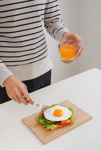 Hands of man cut the eggs on paper, served with bread, herbs, sausage and fresh juice.