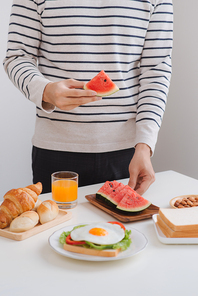 A man eating breakfast at home in morning with sandwich and fruit.