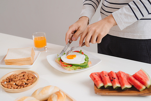 Hands of man cut the eggs on paper, served with bread, herbs, sausage and fresh juice.