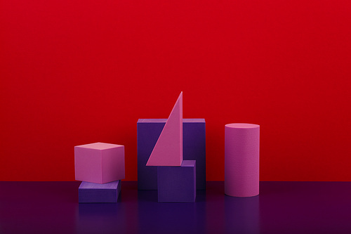 Still life with geometric composition with purple figures on purple shiny table against red background with copy space. High quality photo