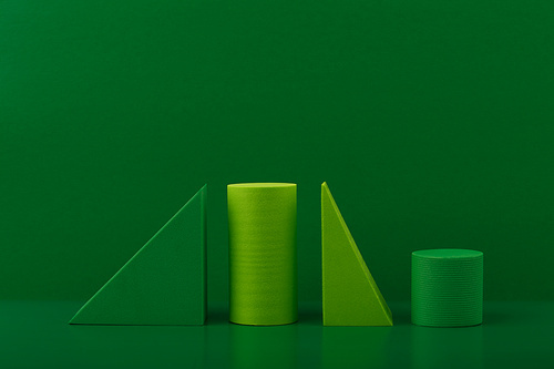 Abstract still life with light and dark green geometric figures triangles and cylinders against green background.