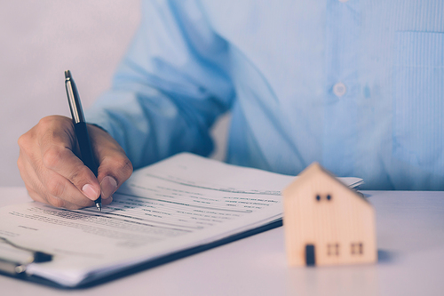 Real estate agent holding home and signing contract about agreement of real property on desk, house broker and planning investment, businessman writing on document form rent house, business concept.