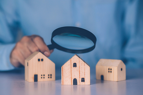 Hand of businessman hold magnifying glass looking house for examining and analyzing quality, inspection and choice home, purchase and search residential and investment, business and property concept.