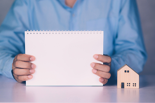 Hands of businessman holding blank notebook and home model, finance and residential, loan and mortgage of real estate, property and residence, investment with financial, business concept.