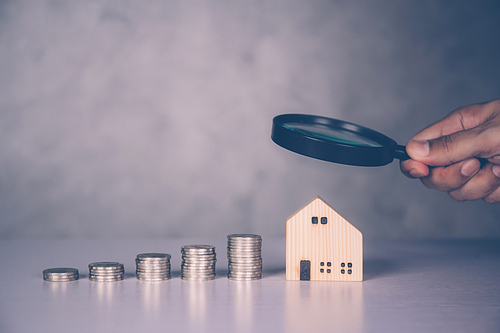 Hands of businessman holding magnifying glass home model with search real estate and property investment for profit, planning of residential and income, loan and mortgage, business concept.