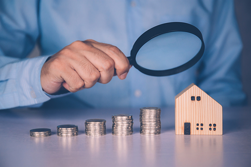 Hands of businessman holding magnifying glass home model with search real estate and property investment for profit, planning of residential and income, loan and mortgage, business concept.