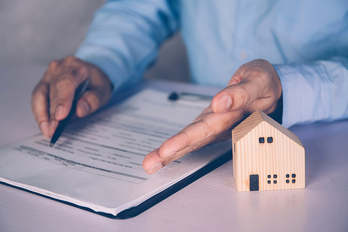 Real estate agent holding home and signing contract about agreement of real property on desk, house broker and planning investment, businessman writing on document form rent house, business concept.