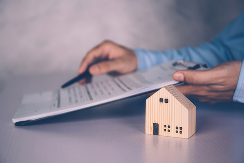 Real estate agent holding home and signing contract about agreement of real property on desk, house broker and planning investment, businessman writing on document form rent house, business concept.