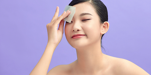 woman with natural face makeup, holding facial oil blotting paper,