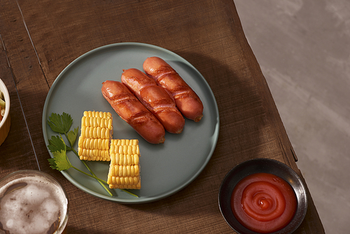 Home grilled sausages on a dark plate, a meat dish on a dark wooden background, hot sausages with spices and salt in a home kitchen, copy space, rustic style, art