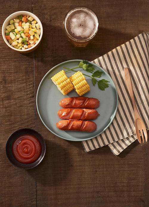 Home grilled sausages on a dark plate, a meat dish on a dark wooden background, hot sausages with spices and salt in a home kitchen, copy space, rustic style, art